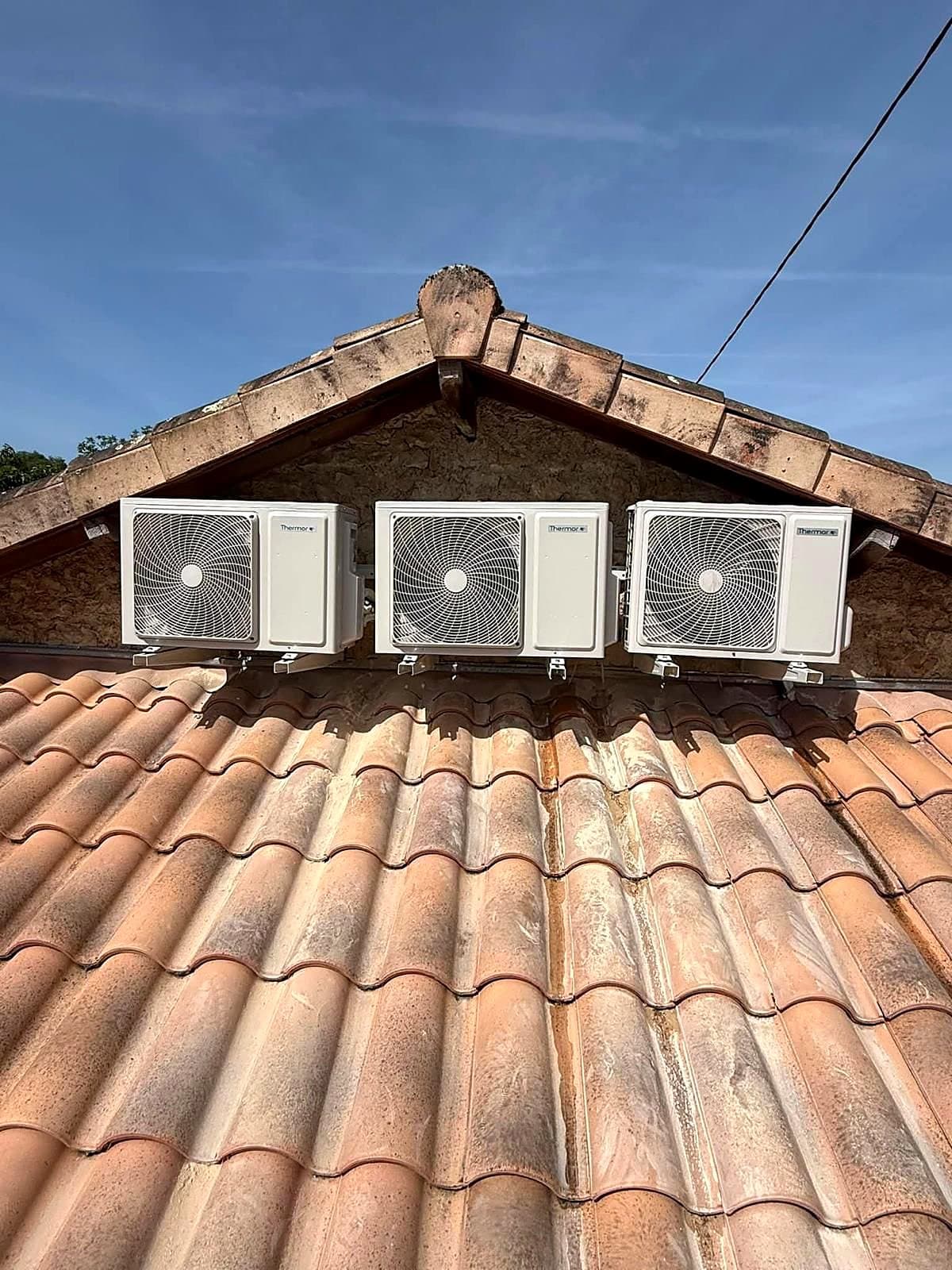 Trois unités extérieures de climatisation fixées en façade sous la toiture
