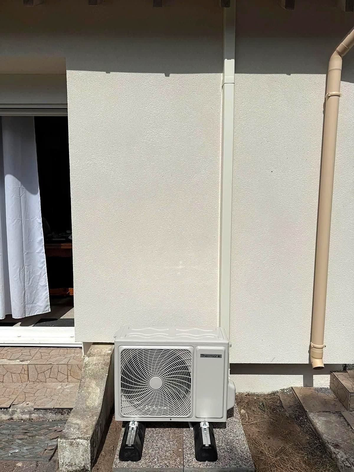 Unité extérieure de climatisation sur supports, au pied d'un mur