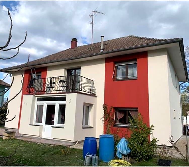 Après : La même maison après isolation par l'extérieur, enduit blanc et bande rouge