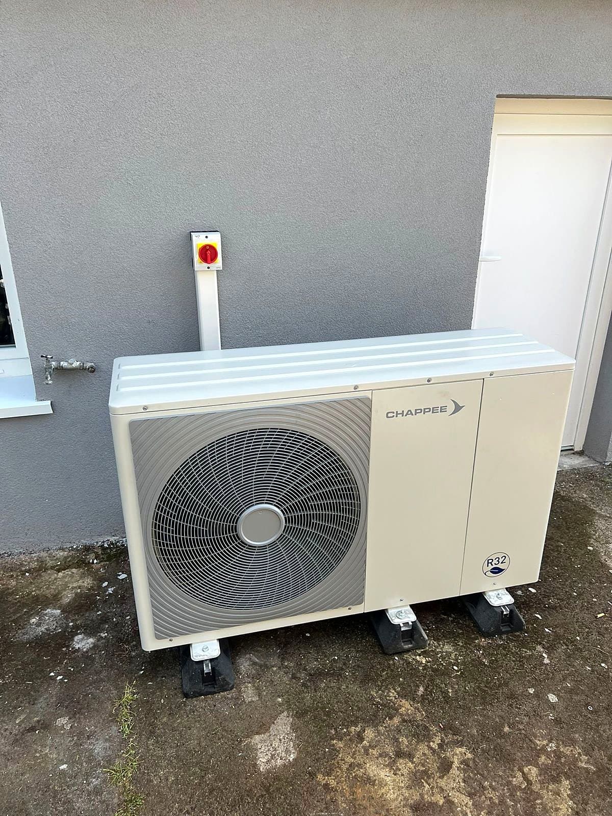 Unité extérieure de pompe à chaleur air/eau posée sur supports, contre une façade
