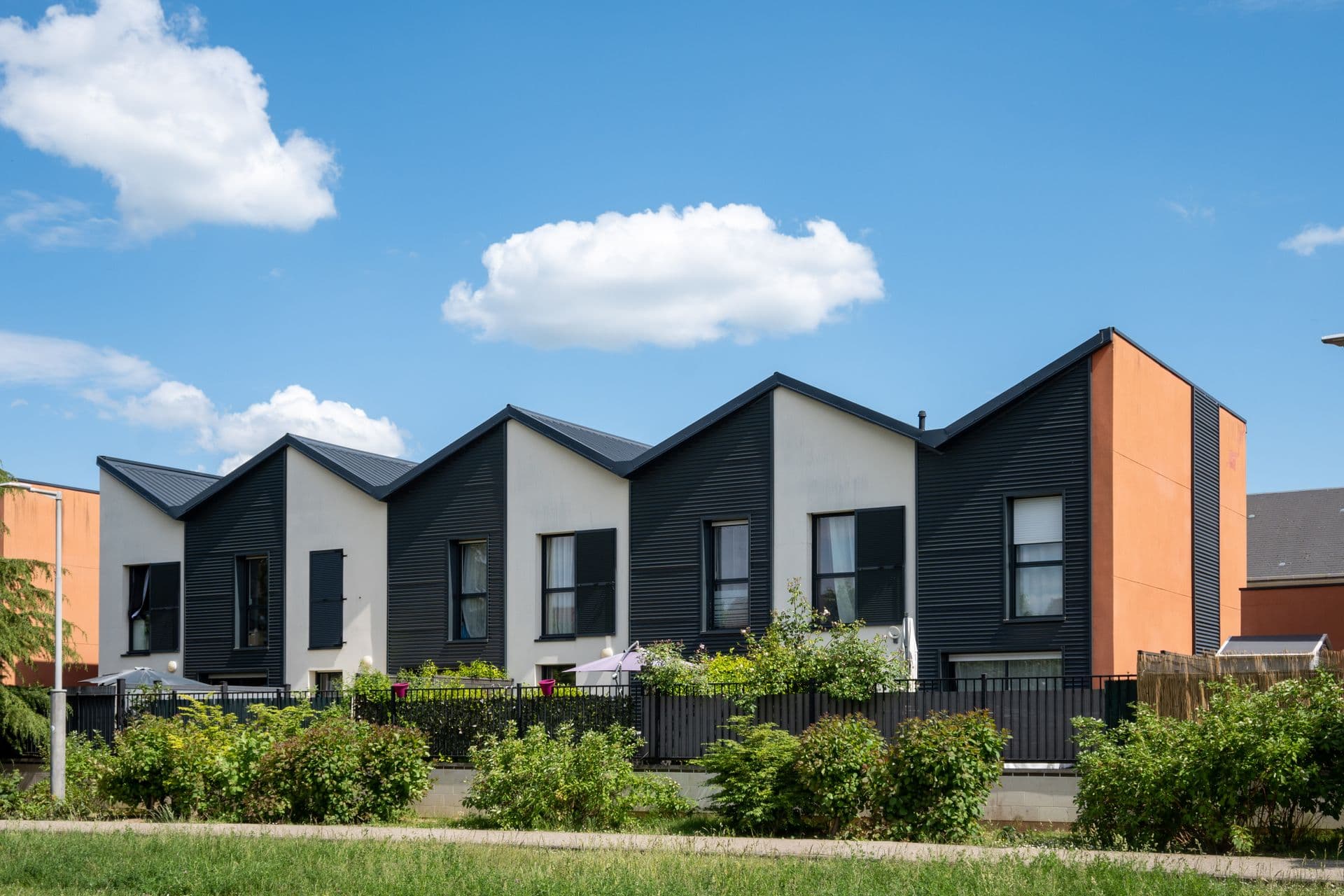 Alignement de maisons contemporaines à pignons, bardage sombre et enduit clair